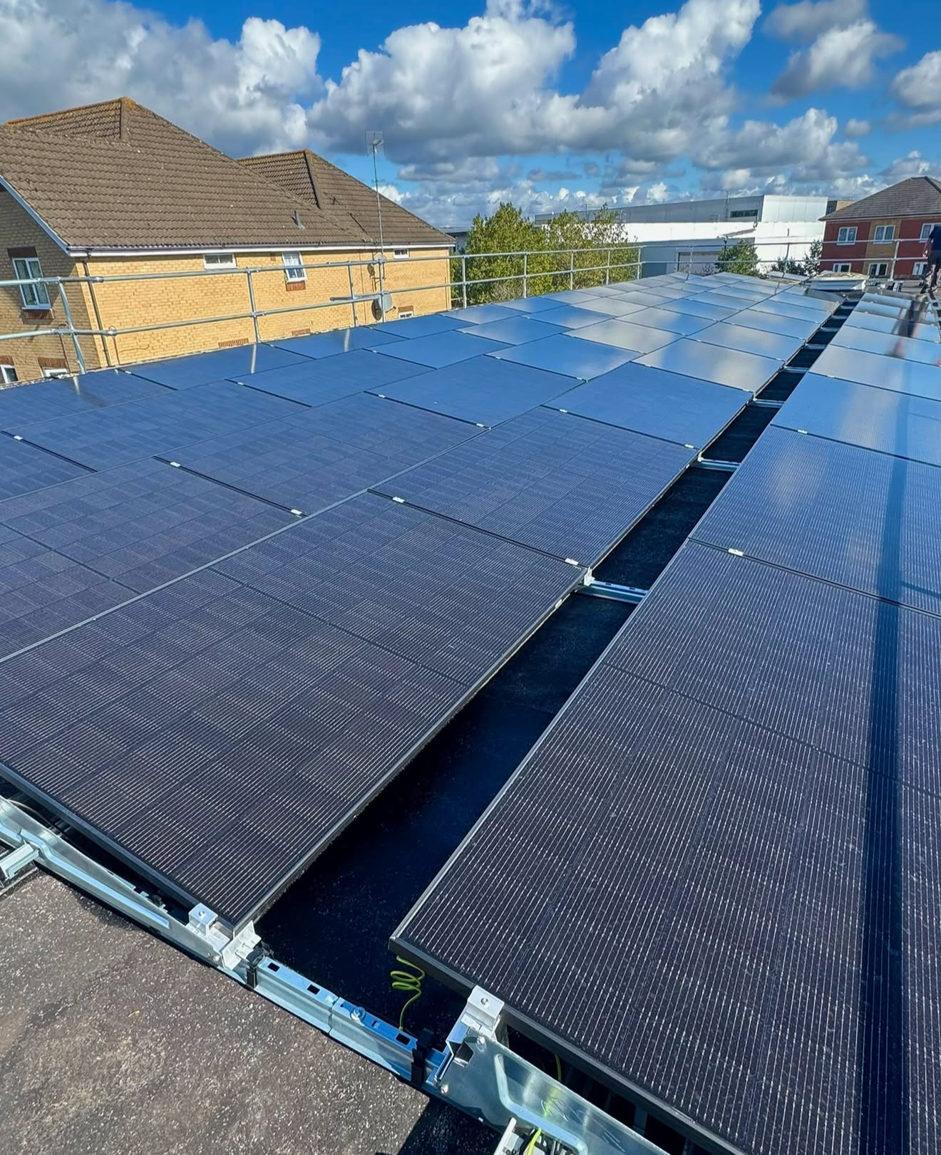 Rows of dark solar panels on a large flat commercial roof with mounting frames and blue sky