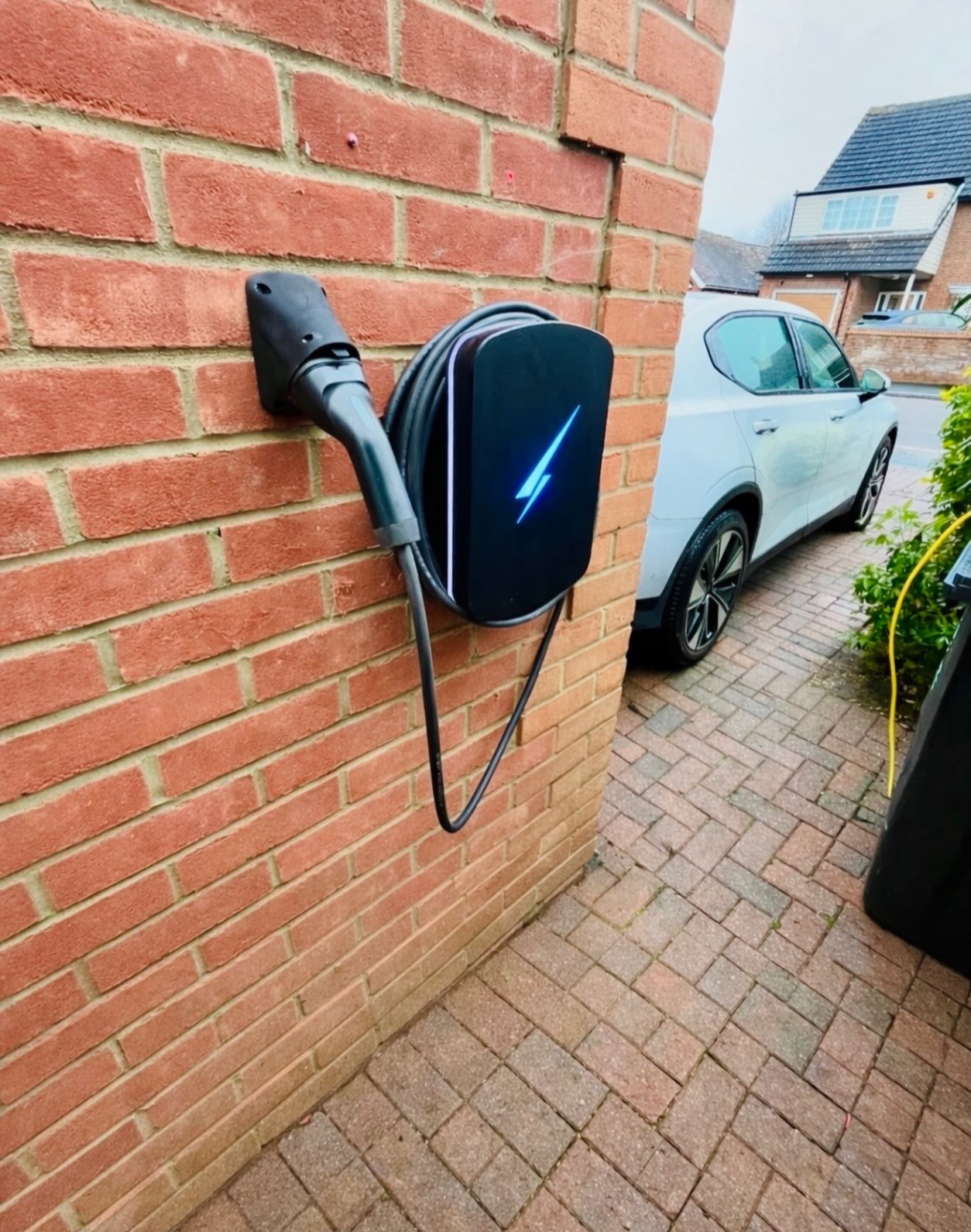 Tethered EV charger with cable holder mounted on a red brick wall
