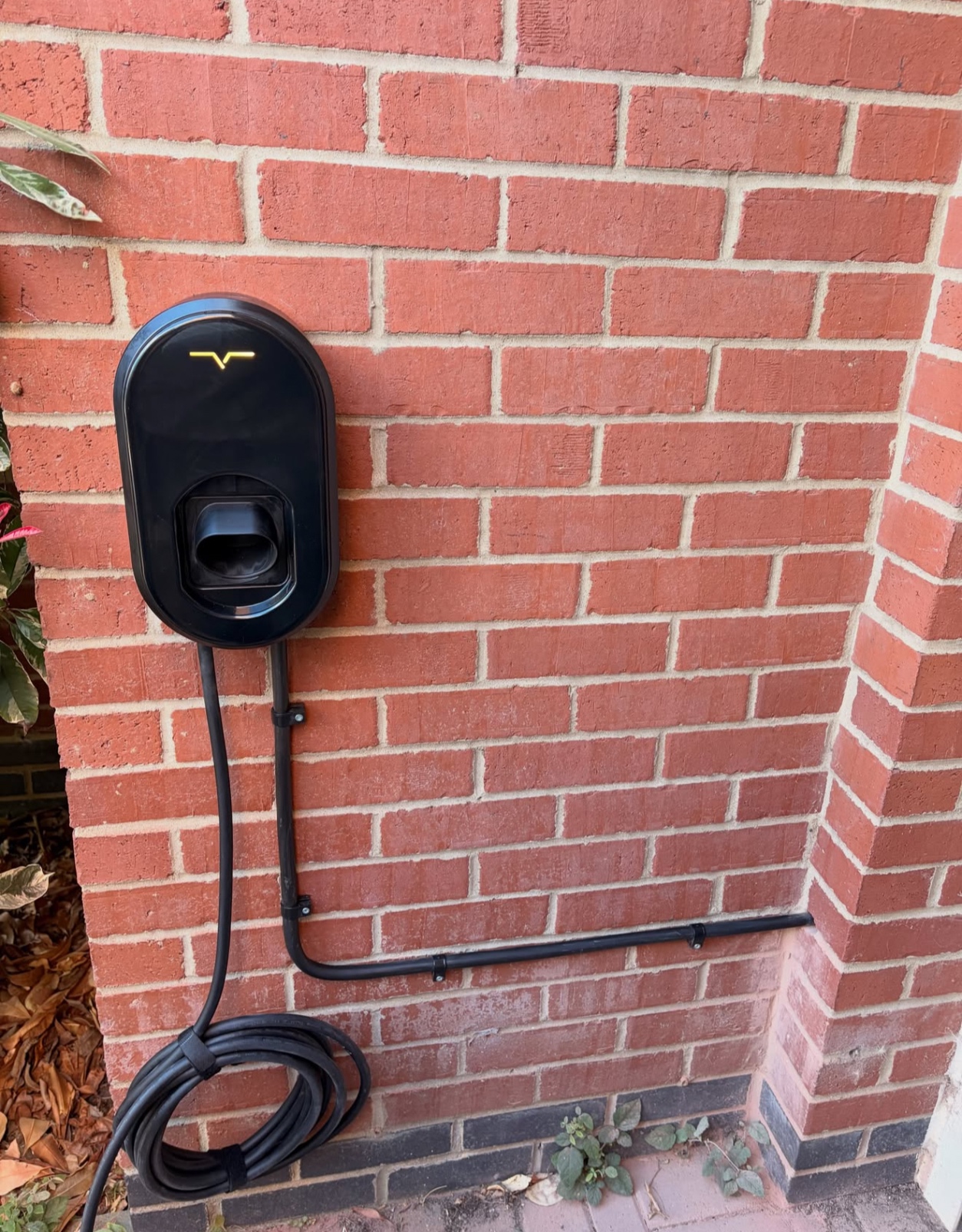 Compact black EV charger mounted on a red brick wall