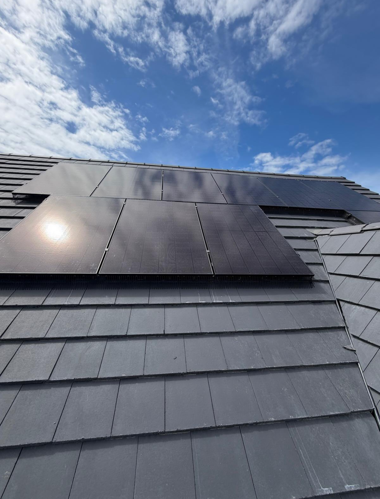 Black solar panels fitted around roof lights on a slate roof