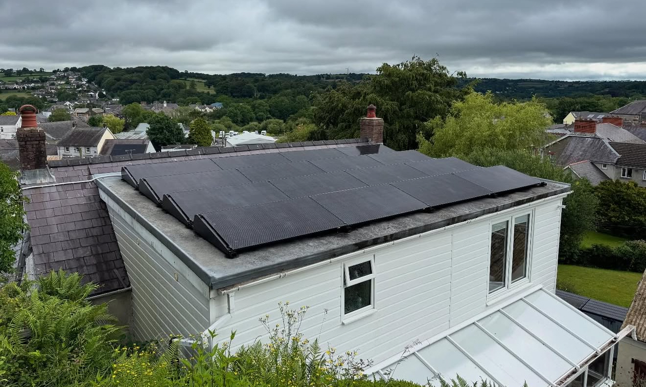 Flat-roof solar installation above a white house in a hilly town