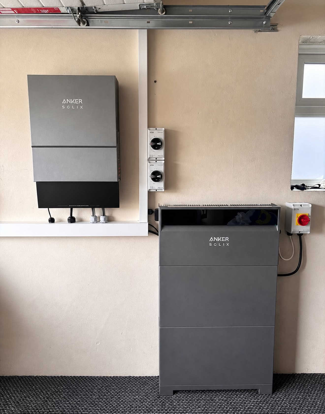 Wall-mounted inverter beside a floor-standing battery inside a garage